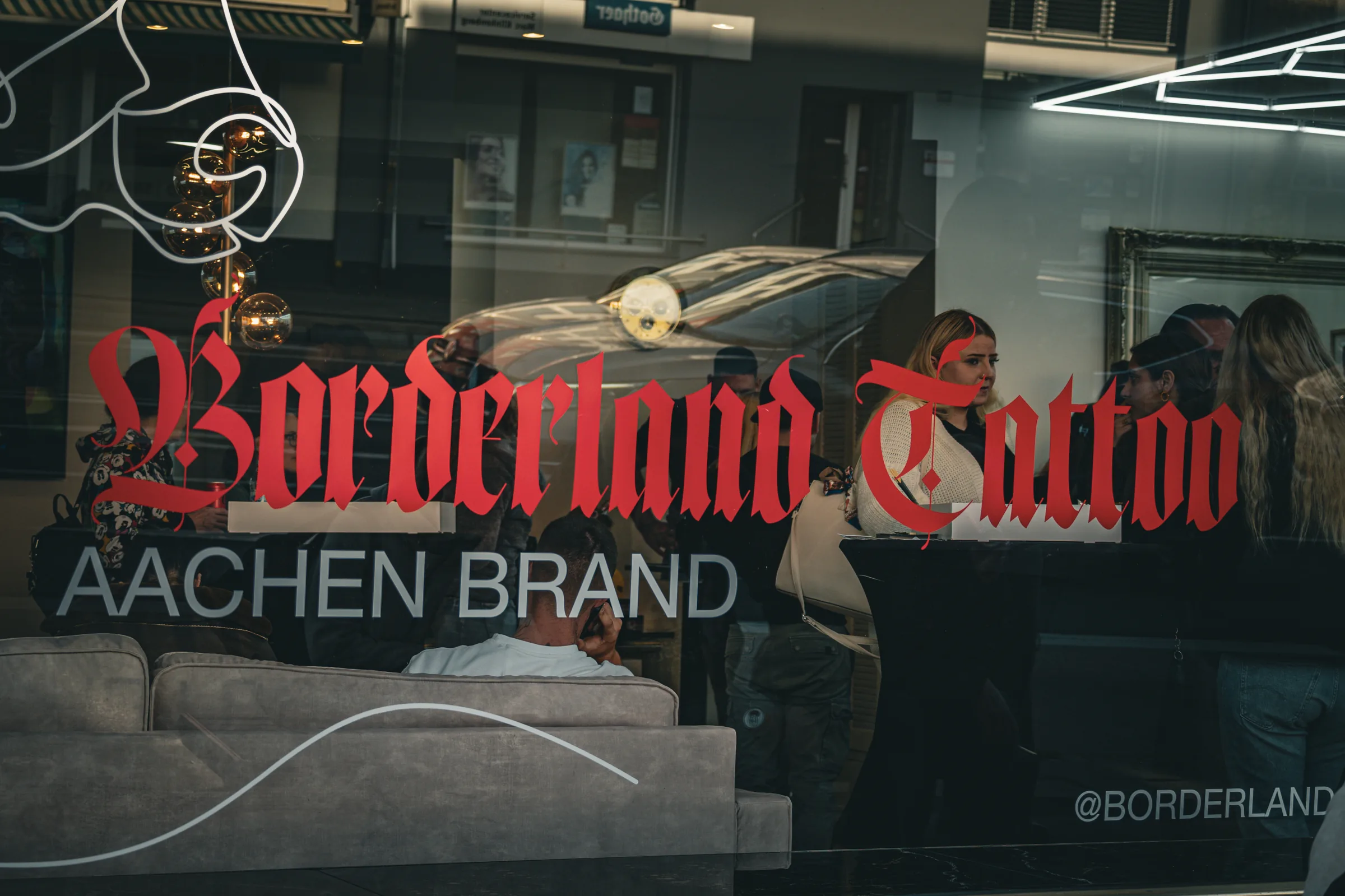 Schaufenster mit rotem Borderland-Tattoo-Schriftzug und Aachen-Brand-Spiegelung — Neueröffnung Borderland Tattoo Aachen, Event-Reportage, Foto eoglou media design Aachen